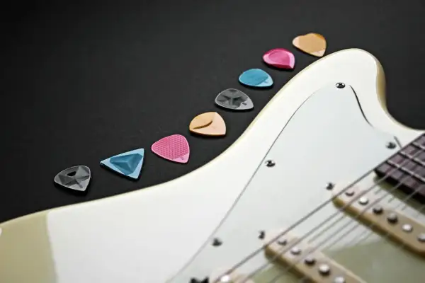 Kolorowe kostki do gitary ułożone wzdłuż białego korpusu instrumentu. Idealne akcesoria, by zacząć naukę gry na gitarze.
