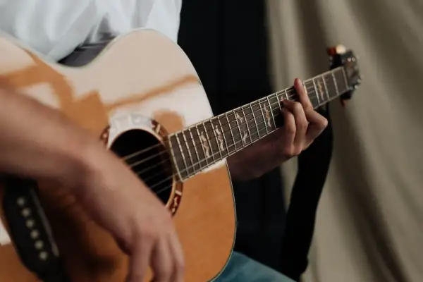 Dłoń grająca na gitarze akustycznej. Zastanawiasz się, ile trwa nauka gry na gitarze? To zależy od Ciebie!