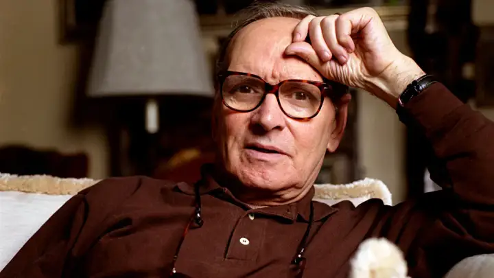 Ennio Morricone, genius kompozytor muzyki do **ennio morricone filmy**, zamyślony z ręką na czole.
